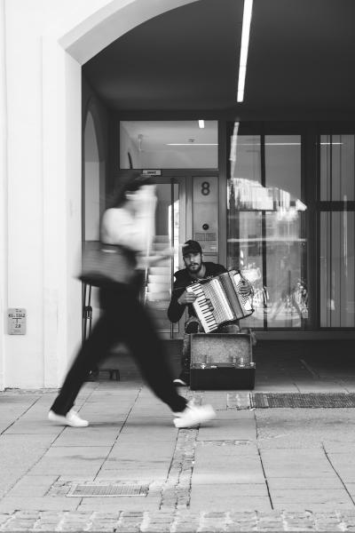 Mann spielt Akkordeon hinter vorbeigehender Frau